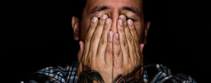 man wearing black, white, and gray plaid sport shirt covering his face