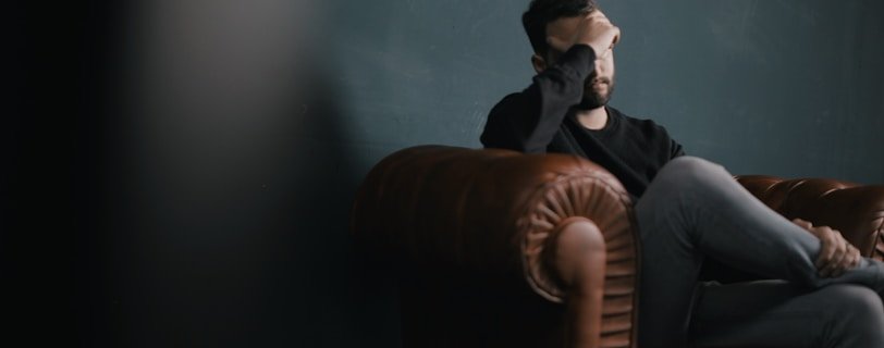 a man holds his head while sitting on a sofa