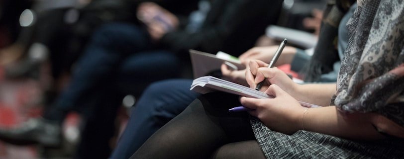 selective focus photography of people sitting on chairs while writing on notebooks