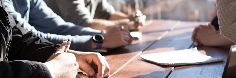 people sitting on chair in front of table while holding pens during daytime