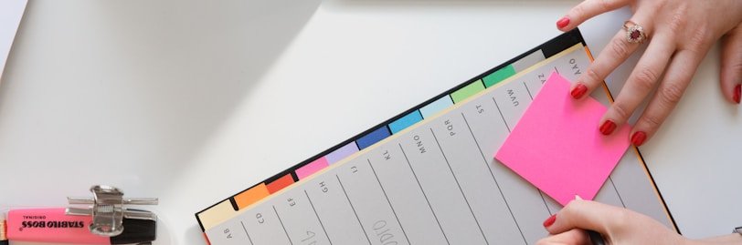 person holding pencil and stick note beside table