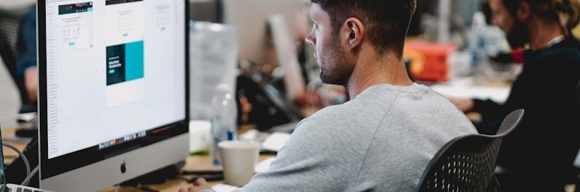 man in gray sweatshirt sitting on chair in front of iMac