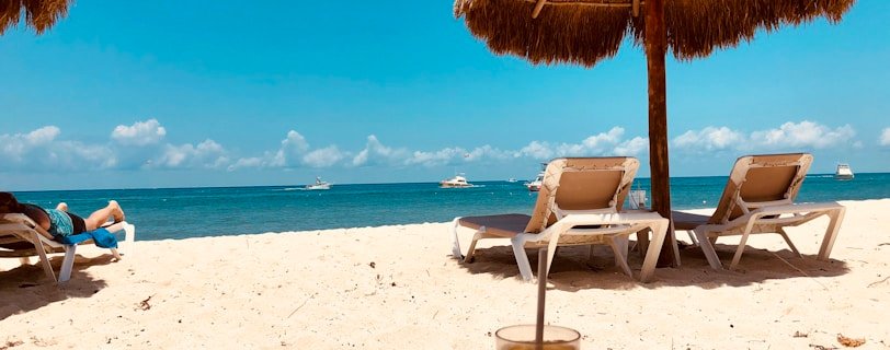 brown parasol and two beach chairs on beach sand
