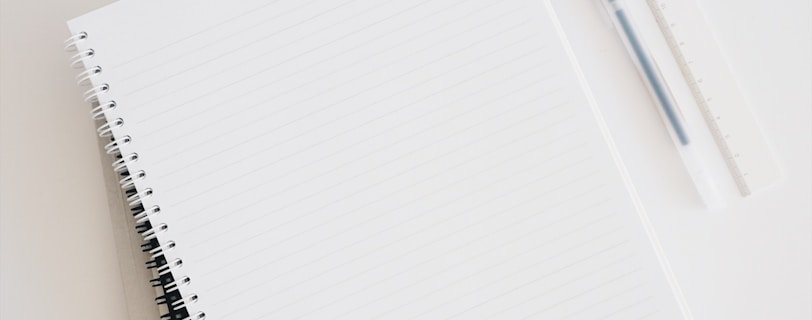 empty spiral notebook near keyboard and pen