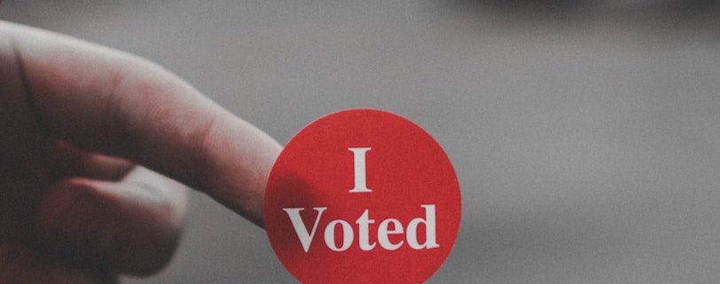 a hand holding a red button that says i vote