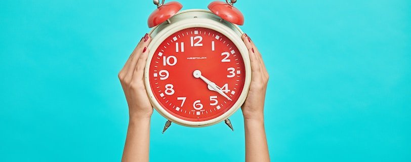 person holding red and beige twin bell analog alarm clock