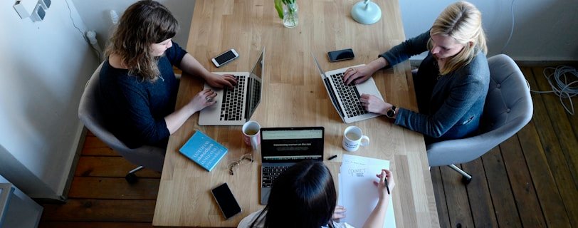 three women sitting around table using laptops