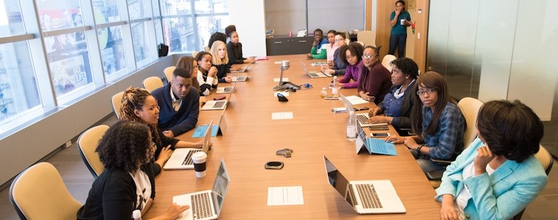 people sitting beside rectangular brown table with laptops