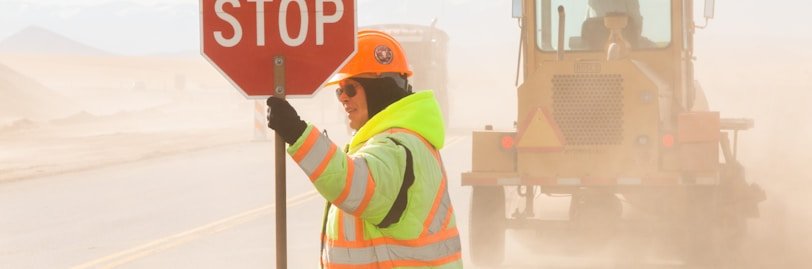 man in green and yellow jacket holding stop sign